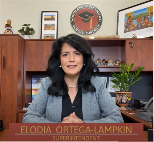 Superintendent Elodia Ortega-Lampkin sitting behind her desks with her hands together on the desk and smiling
